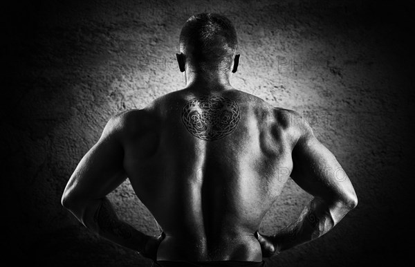 Huge weightlifter stands with his back to the camera and shows his huge back. Back view