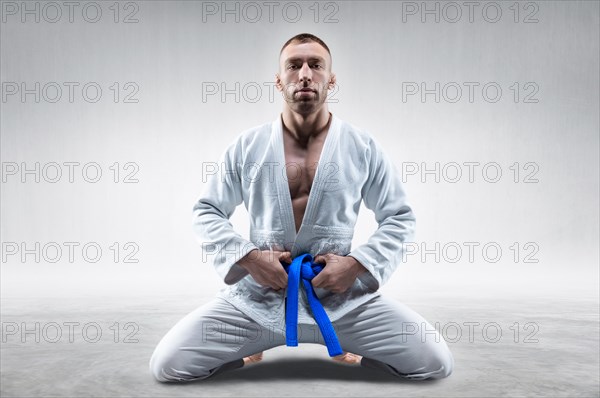 Athlete in a kimono with a blue belt sits and waits for the opponent. Concept of karate