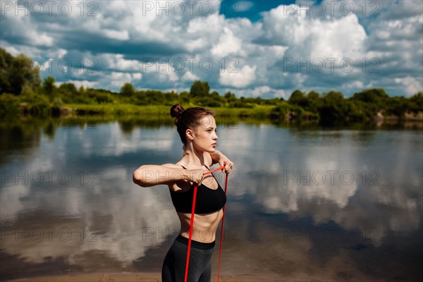 Athletic woman goes in for sports in nature in summer on the beach with resistance band