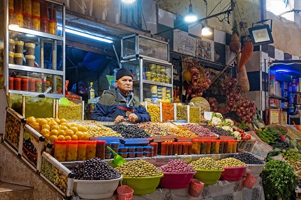 Moroccan vendor selling table olives at food market in the city Meknes