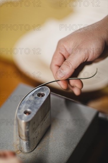 Unrecognizable luthier lute maker artisan both hands performing bend controller purfling strips process in iron tool for a new raw back and front plates of classic handmade violin in his workshop in C...