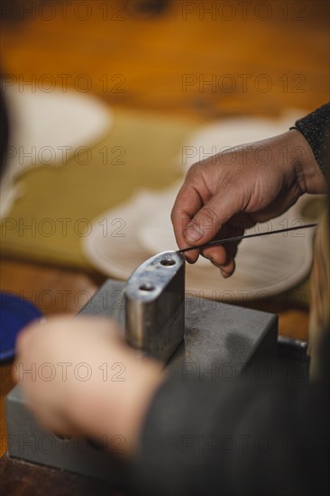 Unrecognizable luthier lute maker artisan hands in his workshop performing bend controller purfling strips process in iron tool for a new raw back and front plates of classic handmade violin in Cremon...