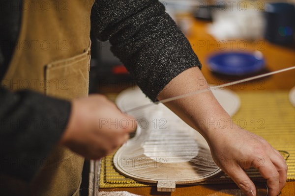 Unrecognizable luthier lute maker artisan both hands performing bend controller purfling strips process in iron tool for a new raw back and front plates of classic handmade violin in his workshop in C...