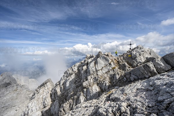 Mountaineer on the rocky summit of the Watzmann Mittelspitze with summit cross, Watzmann crossing,