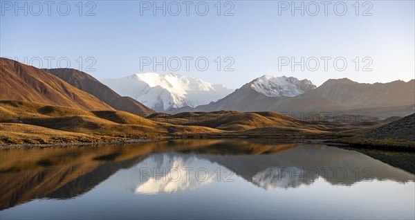 White glaciated and snowy mountain peak Pik Lenin at sunset, mountains reflected in a lake between