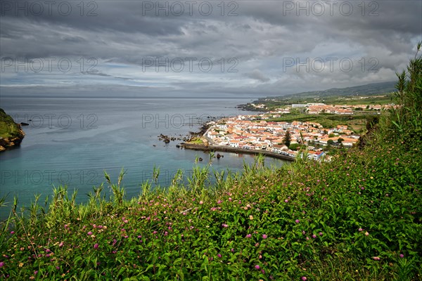 View of the town of Horta surrounded by green hills and cliffs under a cloudy sky, Monte da Guia,