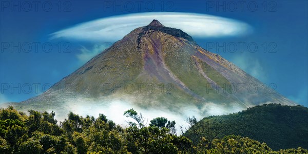 Pico volcano with a lenticularis cloud in the blue sky, surrounded by vegetation, Gruta das Torres,