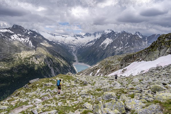 Two mountaineers on hiking trail, view of Schlegeisspeicher, glaciated rocky mountain peaks Hoher