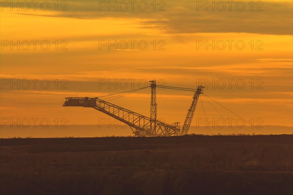 Silhouette of a large conveyor bridge against the orange-coloured evening sky, open-cast lignite