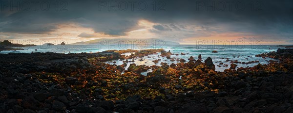 Panoramic coastal view of the town of Madalena at sunset with rocky volcanic and the island of