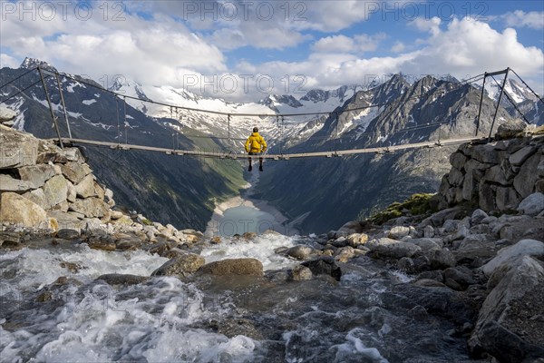 Mountaineer sitting on a suspension bridge over a mountain stream Alelebach, picturesque mountain