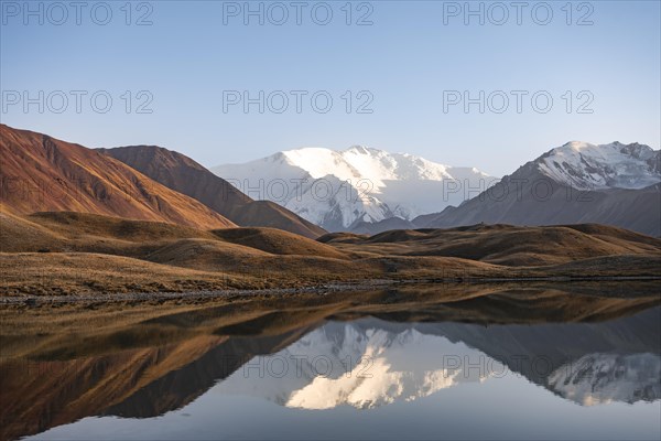 White glaciated and snowy mountain peak Pik Lenin at sunset, mountains reflected in a lake between