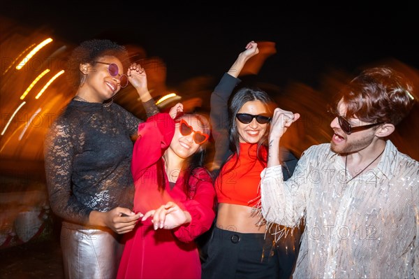 Night photo with flash and motion of a group of excited multi-ethnic friends dancing in the street