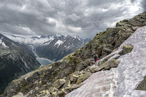 Mountaineer on hiking trail with snow, view of Schlegeisspeicher, glaciated rocky mountain peaks