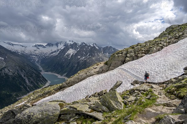 Mountaineer on hiking trail with snow, view of Schlegeisspeicher, glaciated rocky mountain peaks