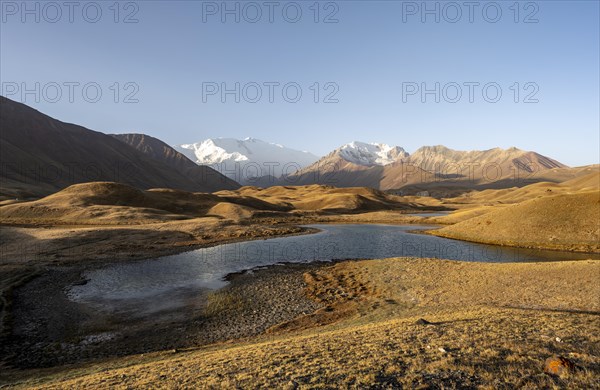 White glaciated and snowy mountain peak Pik Lenin at sunrise, mountains reflected in a lake between