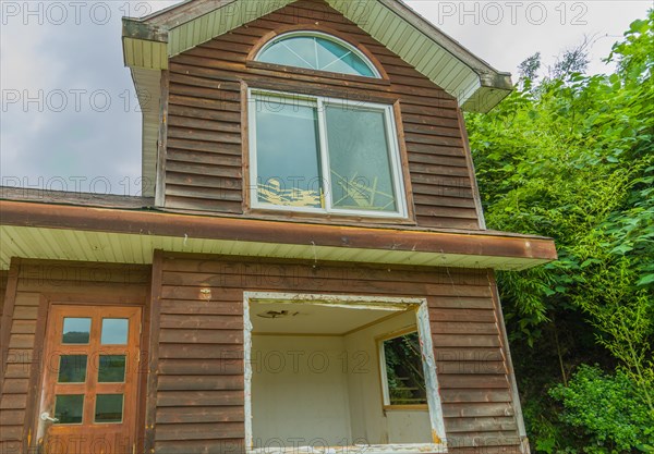 View of window on second story, front door and first floor window frame of abandoned house in