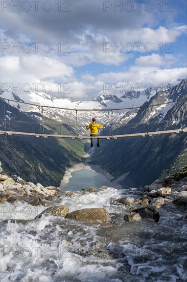 Mountaineer sitting on a suspension bridge over a mountain stream Alelebach, picturesque mountain