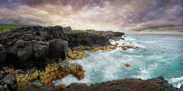 View of the wild coastline with rugged cliffs of lava rock and roaring waves under a grey sky,