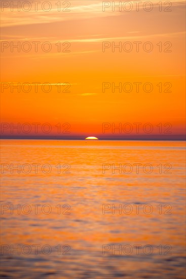 Intense, atmospheric sunset with bright orange-yellow sky over the Baltic Sea, only a small part of