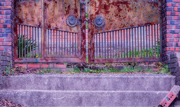 View of stairs leading to a chained rusted gate with red brick columns on each side located at old