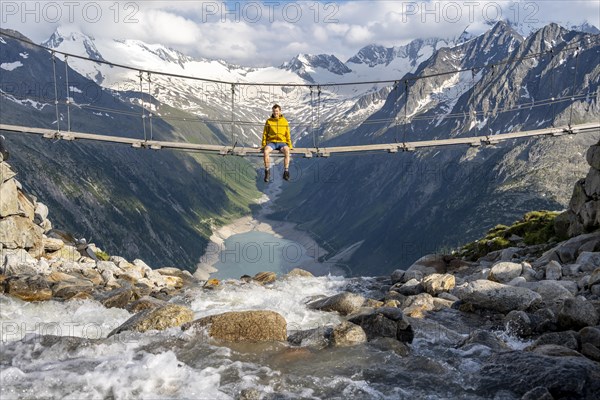 Mountaineer sitting on a suspension bridge over a mountain stream Alelebach, picturesque mountain