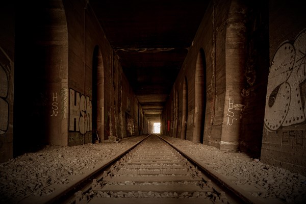 An abandoned railway tunnel, symmetrical with rails and side walls full of graffiti, former Rethel