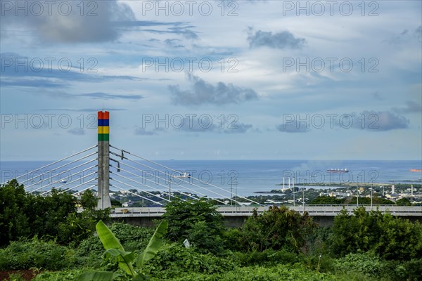 A highway with Mauritian emblem on pillar and a truck driving, surrounded by mountains and an