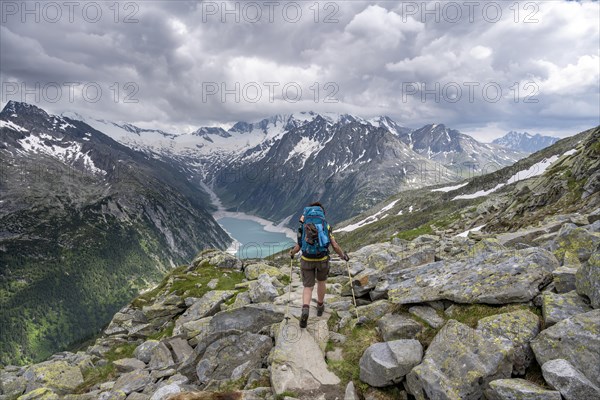Mountaineer on hiking trail, view of Schlegeisspeicher, glaciated rocky mountain peaks Hoher