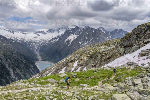 Two mountaineers on hiking trail, view of Schlegeisspeicher, glaciated rocky mountain peaks Hoher