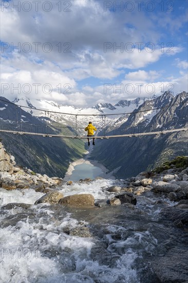 Mountaineer sitting on a suspension bridge over a mountain stream Alelebach, picturesque mountain