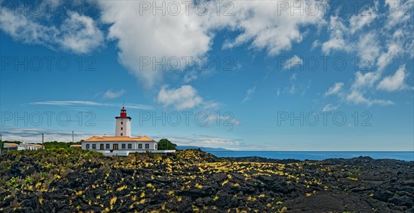 Wide lava flow with the striking lighthouse Farol da Ponta da Iha in front of a blue sky with white