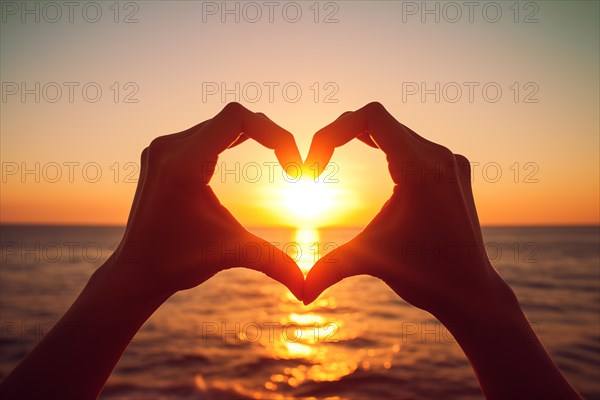 Two hands forming a heart shape, silhouetted against a breathtaking ocean sunset. Love and warmth