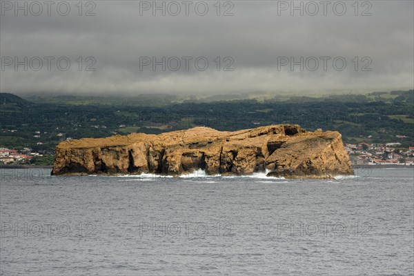 The remote rocky island 'Iieu Deitado' off a coastline of Pico under a cloudy sky, Iieu Deitado,