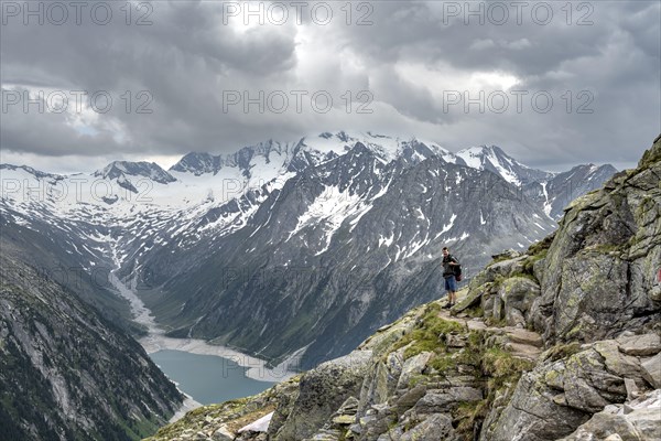 Mountaineer on hiking trail, view of Schlegeisspeicher, glaciated rocky mountain peaks Hoher