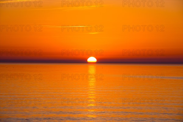 Intense, atmospheric sunset with bright orange-yellow sky over the Baltic Sea, reflection of the