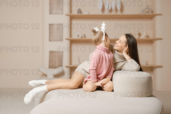 A mother and daughter sit together in a cozy living room with a beige walls. The daughter is