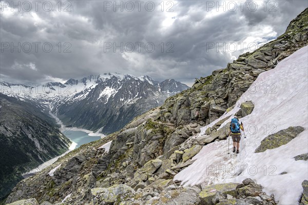 Mountaineer on hiking trail with snow, view of Schlegeisspeicher, glaciated rocky mountain peaks
