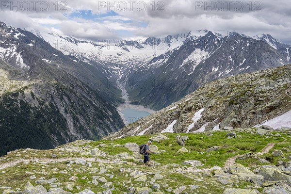 Mountaineer on hiking trail, view of Schlegeisspeicher, glaciated rocky mountain peaks Hoher