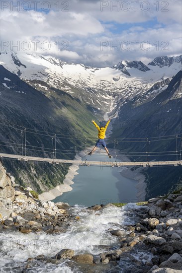 Mountaineer jumping on a suspension bridge over a mountain stream Alelebach, picturesque mountain