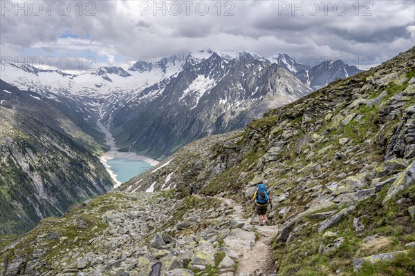 Mountaineer on hiking trail, view of Schlegeisspeicher, glaciated rocky mountain peaks Hoher