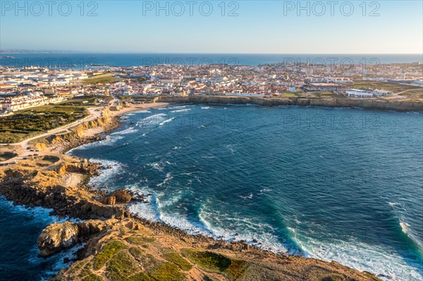 Drone view of waves break on rocky shores in town of Peniche, Portugal. Summer sunset haze, little