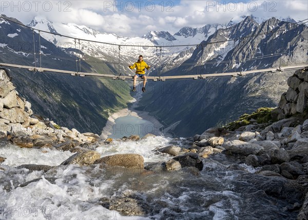 Mountaineer sitting on a suspension bridge over a mountain stream Alelebach, picturesque mountain