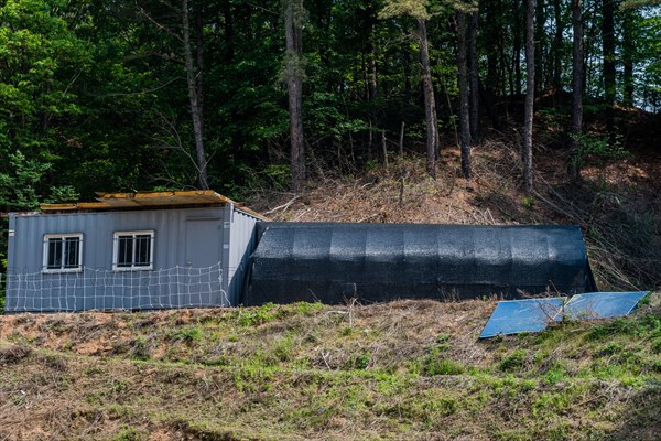 Two storage buildings on hillside in wooded farm region, one metal and one support frame covered