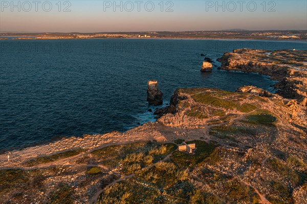 Bird's-eye view of sunset over ocean waves break on rocky shores, Peniche, Portugal. Summer sunset