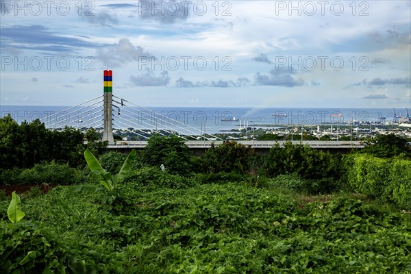 A highway with Mauritian emblem on pillar and a truck driving, surrounded by mountains and an