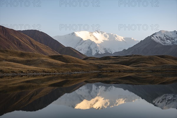 White glaciated and snowy mountain peak Pik Lenin at sunset, mountains reflected in a lake between