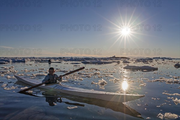 Child paddling in sea kayak through ice floes in the sea, kayak, backlight, sunbeams, summer,