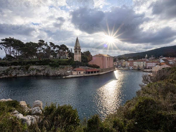 Sun breaking through clouds, view of the harbour entrance of Veli Losinj, with St. Anthony's