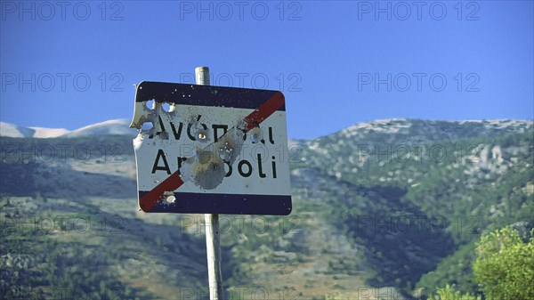 A damaged road sign with bullet holes, in the background a picturesque mountain landscape,